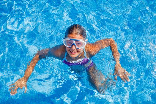 Cute happy young girl in goggles swimming and snorking in the swimming pool