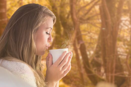 Pretty blonde relaxing on the couch with tea against tranquil autumn scene in forest
