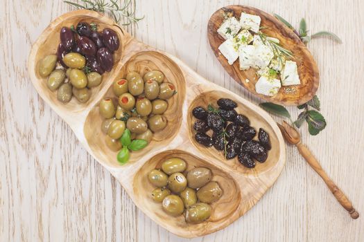 Assorted olives and feta or goat cheese cheese in olive tree dish on wooden table