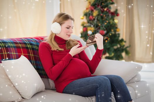 Composite image of pregnant woman looking at baby shoes sitting on sofa