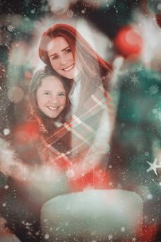 Composite image of festive mother and daughter wrapped in blanket