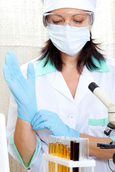 a female medical or scientific researcher or woman doctor looking at a test tube of yellow solution in a laboratory and putting on gloves 