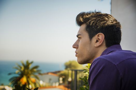 Attractive young man outdoor looking over a seaside landscape with sea in background with a serious expression