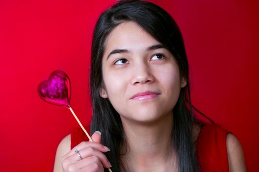 Beautiful biracial young teen girl holding heart balloon, smilin
