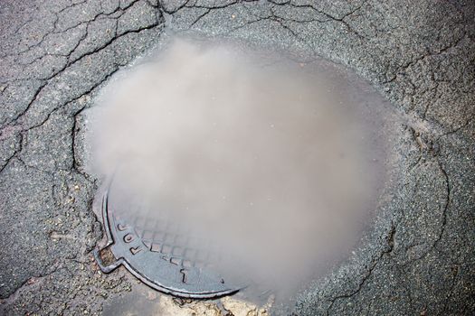 The puddle on the manhole in asphalt surface
