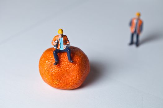 Miniature people in action and man sitting on an orange