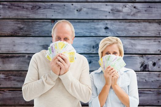 Happy mature couple smiling at camera showing money against grey wooden planks