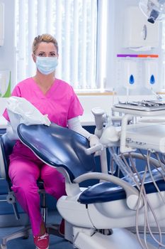 Dentist in pink scrubs looking at camera beside chair at the dental clinic