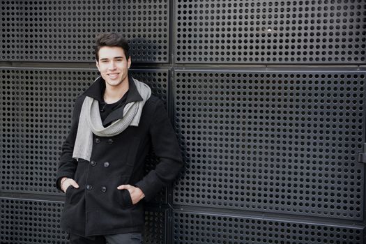Trendy young man in winter fashion against wall in urban environment