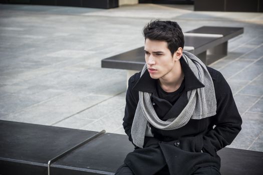 Trendy handsome young man sitting on stone bench