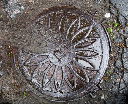 Manhole with wet metal cover in the cracked asphalt surface