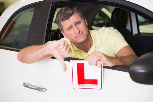 Man gesturing thumbs down holding a learner driver sign at new car showroom
