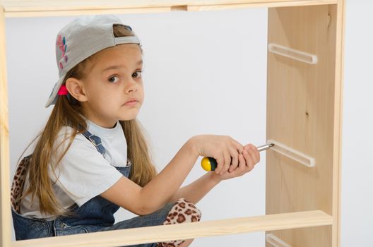 Girl-collector of furniture with a screwdriver collects wooden cabinet