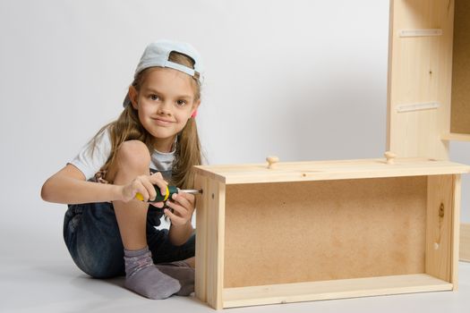 Little girl in overalls collector collects furniture drawer of the dresser