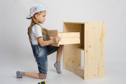 Girl in overalls furniture assembler inserts a drawer chest of drawers