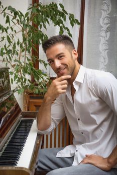 Young handsome male artist sitting at wooden classical upright piano