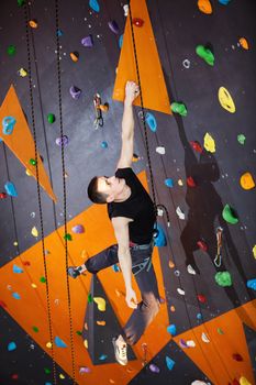 Young man practicing rock-climbing in climbing gym