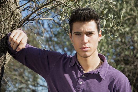 Handsome young man leaning against olive tree