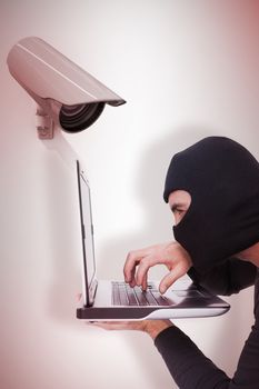 Composite image of focused burglar with balaclava typing on laptop