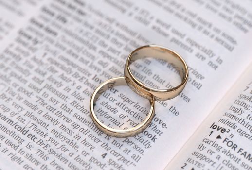 Couple of gold wedding rings on a dictionary page showing love definition 