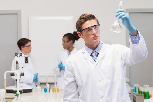 Scientist looking at white precipitate while colleagues talking together 