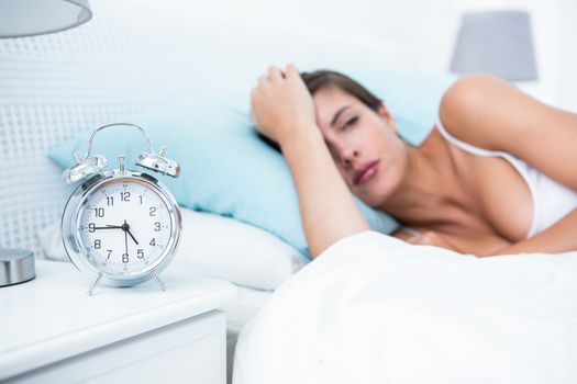 Pretty woman lying in bed with alarm clock