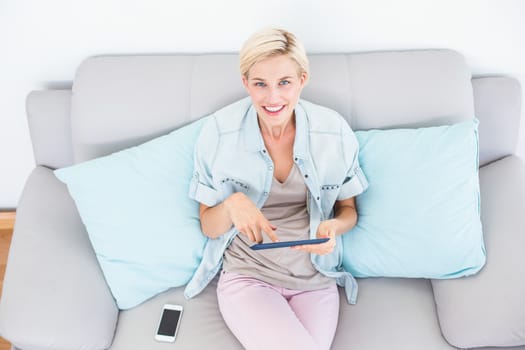 Pretty blonde woman using her tablet on the couch in the living room