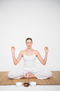 Fit woman meditating on bamboo mat on white background