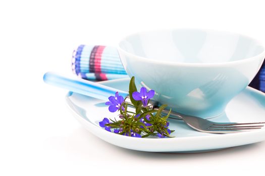 tableware with blue lobelia flowers and cutlery, on a white back