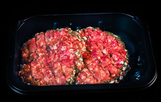 Two raw red burgers in a black plastic tray isolated on black