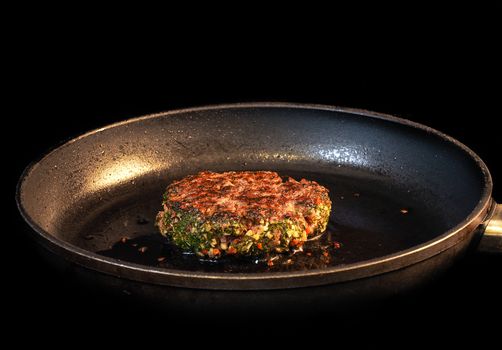 Frying seasoned hamburger in fry pan isolated on black