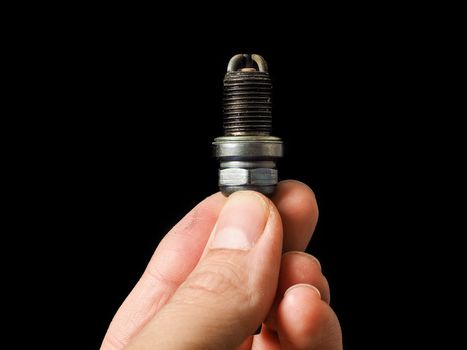 Hand of a male person holding a worn spark plug isolated on blac