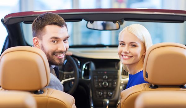 auto business, car sale, consumerism and people concept - happy couple sitting in car at auto show or salon