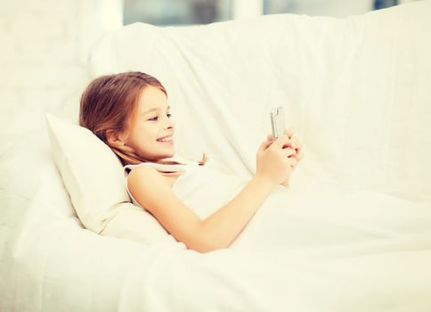 little girl with smartphone playing in bed
