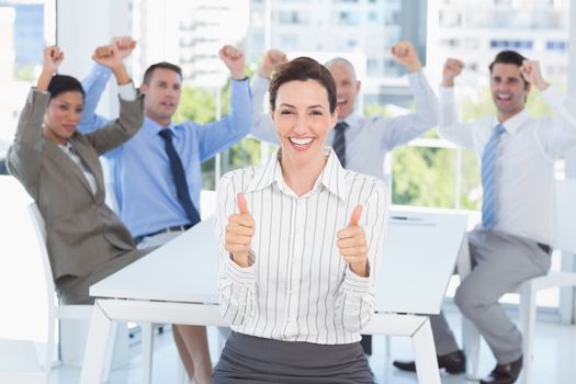 Smiling businesswoman giving thumbs up with her team behind