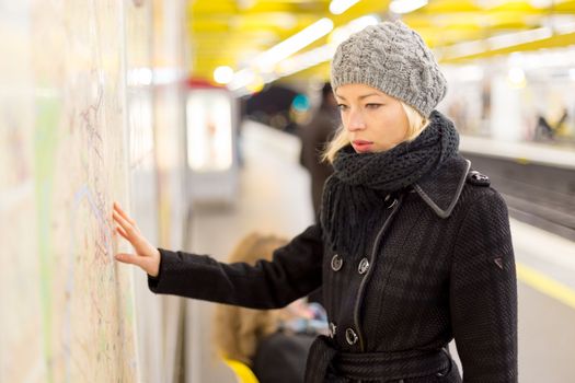 Casually dressed woman wearing winter coat, orientating herself with public transport map panel. Urban transport.