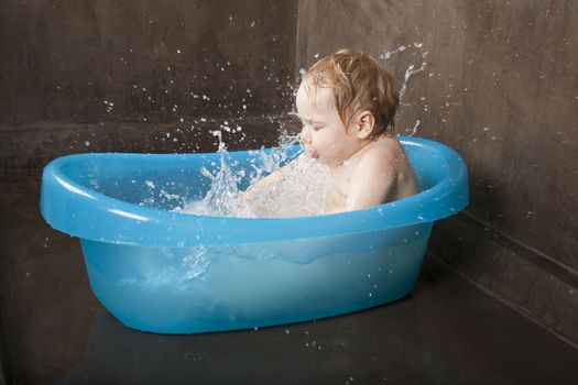 blonde baby splashing in blue little bath indoor