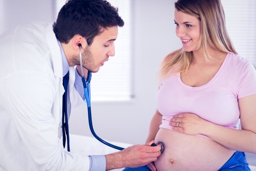 Doctor talking to smiling pregnant patient while examining her stomach