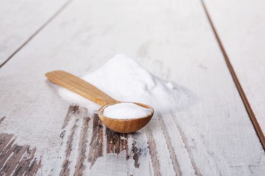 Baking soda on wooden spoon on white wooden textured background.