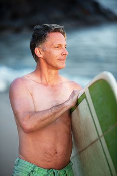 Confident middle aged surfer with surfboard looking over