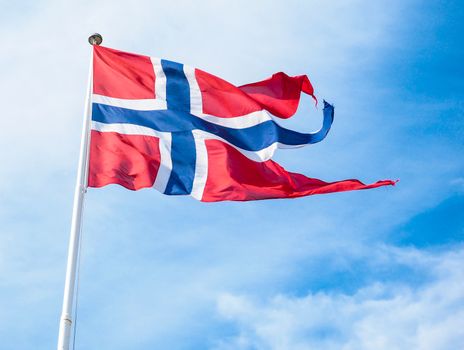 The Royal flag of Norway on a pole towards blue and white sky