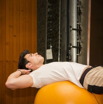 Young man training abs on fitness ball