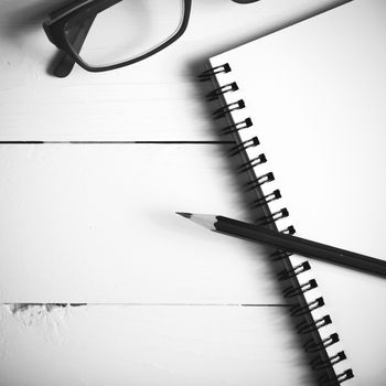 pencil and notepad with eyeglasses over white table view from above black and white color style