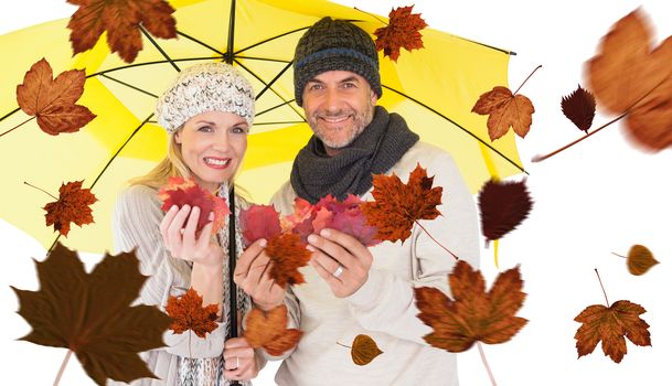 Composite image of portrait of couple holding autumn leaves while standing under yellow umbrella