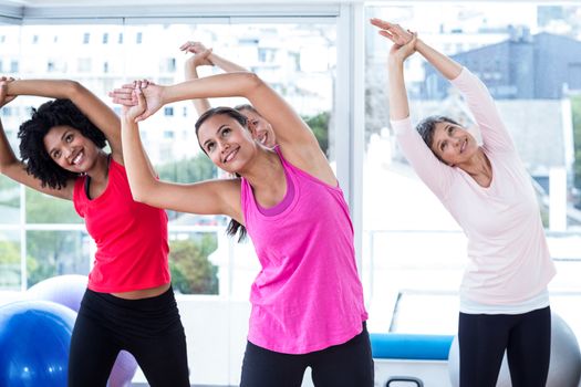 Smiling women exercising with arms raised in fitness studio