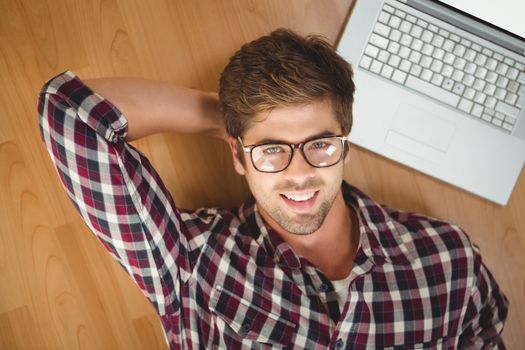 Hipster smiling while lying by laptop on hardwood floor