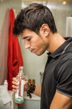 Handsome young man using mouthwash, in bathroom