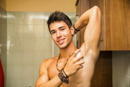 Handsome young man in bathroom, spraying cologne or perfume
