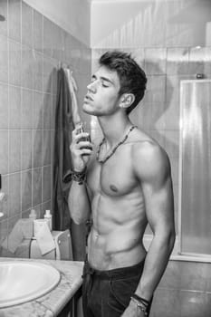 Handsome young man in bathroom, spraying cologne or perfume