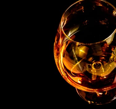 snifter of brandy in elegant typical cognac glass on black background with space for text